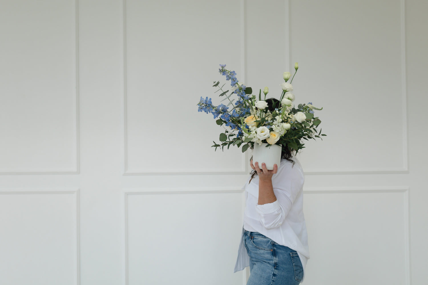 Person holding a bouquet of flowers in front of their face against a white paneled wall