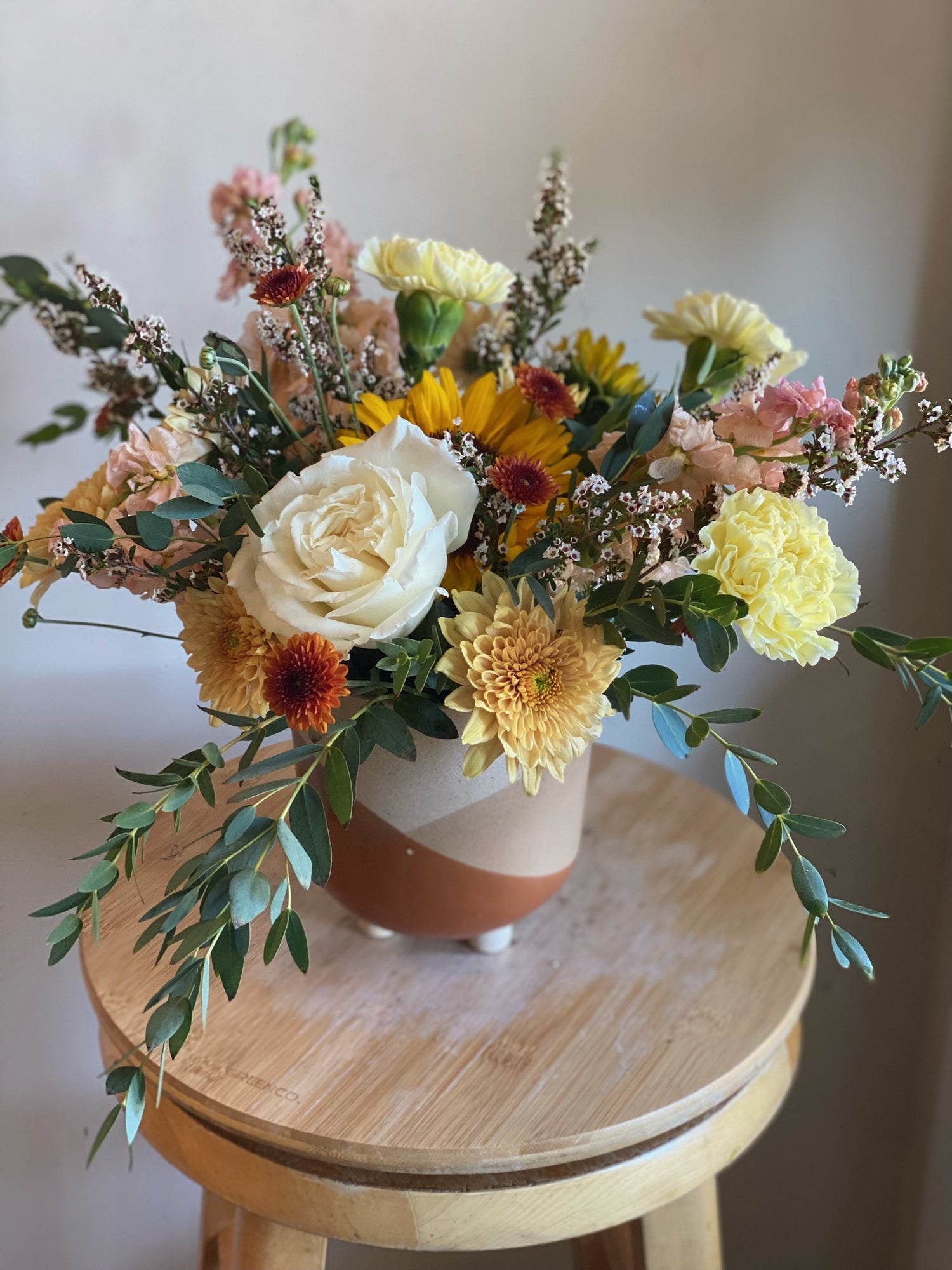 Fall flowers in shades of cream, yellow and dark orange arranged in a ceramic pot